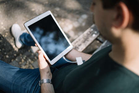 Out of focus young man holding tablet with blank screen. Close-up shoulder view of blurred man holding tablet with black screen outdoor.の写真素材