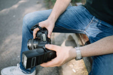 Close-up view of mans hands holding professional camera. Cropped man holding DSLR camera with flash while sitting outdoor.の写真素材