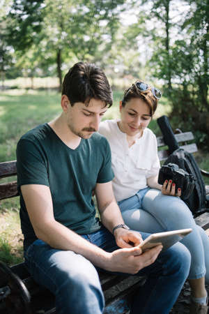 Portrait of woman and male photographer looking at tablet. Man holding tablet while sitting on bench...