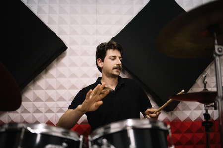 Drummer having fun with drumsticks while playing drums. Male musician recording music while playing...