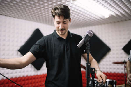 Portrait of smiling man setting microphone on stand. Blurred singer setting cables to his microphone...