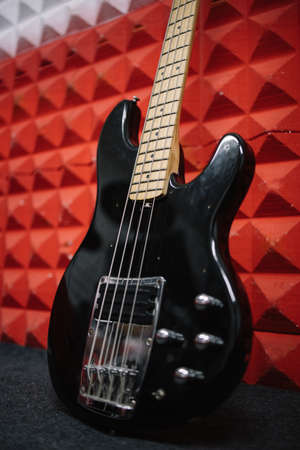 Black electric guitar propped on wall in soundproof studio. Close-up portrait of shiny guitar on wall in music recording studio.の写真素材