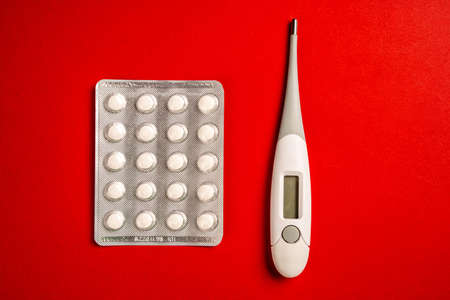 Digital thermometer and pills isolated on red background. Virus accessories for pandemic time isolated on red surface.の写真素材