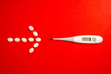 Pills arranged in arrow shape pointing thermometer. Arrow made from arranged pills next to digital...