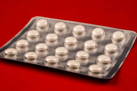 Close-up view of blister with pills isolated on red background. Selective focus of pills against...