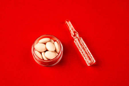 Top view of medical drugs on red background. Jar of pills on red surface with ampoule arranged on red surface.の写真素材