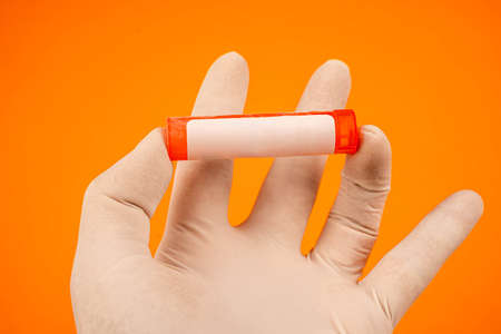 Cropped hand with gloves holding vial with empty label. Top view of hand with white protective...