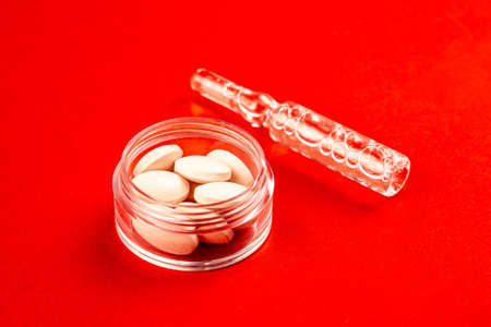 Ampoule next to pills in jar isolated on red background. Close-up view of medical drugs on red...