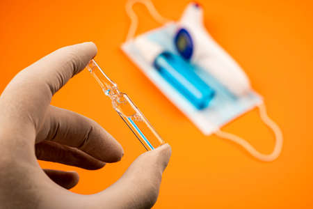 Close-up view of hand with protective gloves holding ampoule. Human hand with gloves holding ampoule...