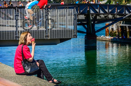 WELLINGTON, NEW ZEALAND - FEBRUARY 03, 2014: Woman in red blouse eating red ice cream at Waterfront lagoon in Wellington, New Zealandのeditorial素材
