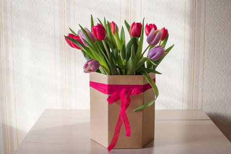 Lilac tulips on a table in a glass vase on a sunny day, a gift from a loved oneの写真素材