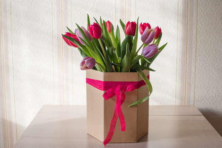 Red and purple tulips on a table in a crafting vase with a ribbon on a sunny day close up, a gift from a loved oneの写真素材