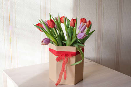 Red and purple tulips on a table in a crafting vase with a ribbon on a sunny day close up, a gift from a loved oneの写真素材