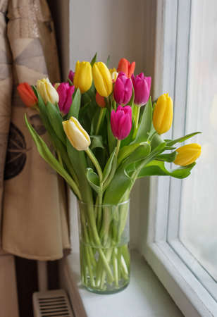 A bouquet of white daisies in a vase on the kitchen table against the background of a window, a refrigerator and stools with a strong blurの写真素材