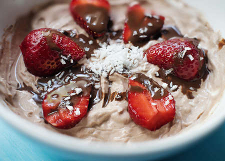 curd dessert with strawberries, chocolate sauce and coconut flakes in white plate on blue wooden backgroundの写真素材