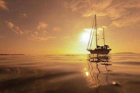 Luxury sailing yacht in front of beautiful golden incredible sunset in tropical ocean. Romantic trip. Summer holiday vacation travel concept. Selective focus.の写真素材