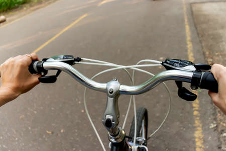 Hands hold the handlebars of the bike. The bike rides on the sidewalk.