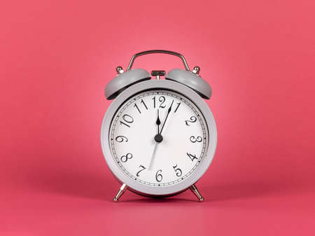 Gray alarm clock with bells, showing twelve as time. Isolated on a watermelon pink background.