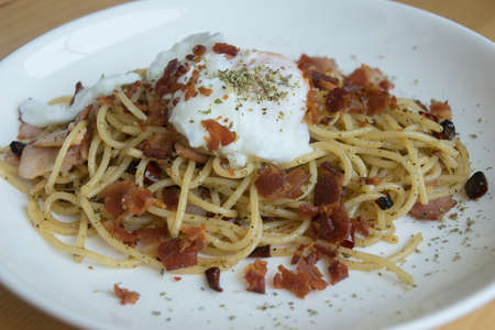 Spaghetti dry chilli with bacon and egg on top on white dishの写真素材
