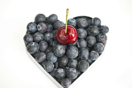 Fresh Blueberries in Heart-Shaped Container with Cherry On Top on White Background