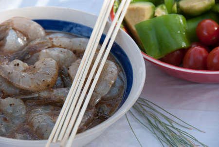 Marinating Shrimp in Bowl with Skewers and Bowl of Chopped Vegetablesの写真素材