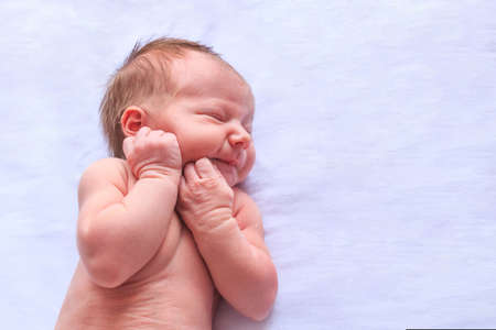 Newborn little baby sleeping on light background and shows emotions, the child wrinkles his noseの写真素材