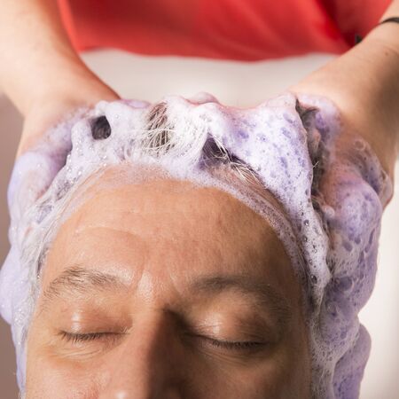 Close up of face of man is getting a hairwash by a hairdresser, with relaxation. The beautician is making foam from shampooの写真素材