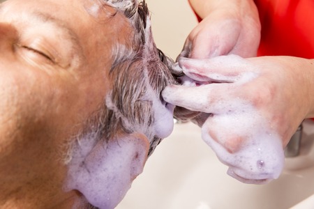 Close up of face of man is getting a hairwash by a hairdresser, with relaxation. The beautician is making foam from shampooの写真素材