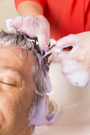 Close up of face of man is getting a hairwash by a hairdresser, with relaxation. The beautician is making foam from shampooの写真素材