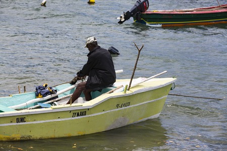 La Trinit , Martinique - April 10, 2017. Old black fisherman in his small wood boat with motor, ready to go to fish, on blue sea.のeditorial素材