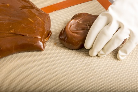 Artisanal production of caramel toffee sweets butterscotch candies. Woman with white lab coat, blouse, cutting rolls of sugar pastry to do butterscotch candies, traditional sweetx of Franceの写真素材