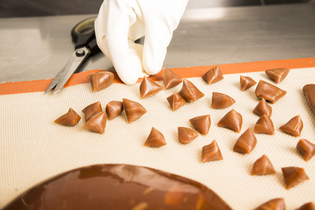 Artisanal production of caramel toffee sweets butterscotch candies. Woman with white lab coat, blouse, cutting rolls of sugar pastry to do butterscotch candies, traditional sweetx of Franceの写真素材