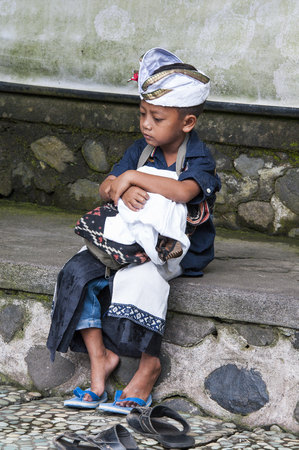 Ubud, Bali, Indonesia - July 30, 2013. Portrait of sad unidentified boy sitting, waiting for his family in the templeのeditorial素材