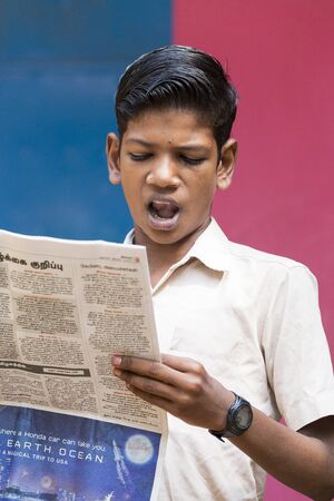 PONDICHERY, PUDUCHERY, INDIA - SEPTEMBER 04, 2017. Young man reads newspaper in the school in front of the other children and teachers. Each monday morning he uses to read the newspaper for world news.のeditorial素材