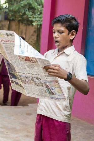 PONDICHERY, PUDUCHERY, INDIA - SEPTEMBER 04, 2017. Young man reads newspaper in the school in front of the other children and teachers. Each monday morning he uses to read the newspaper for world news.のeditorial素材
