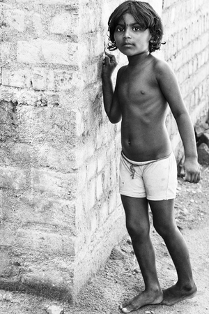 PONDICHERY, PUDUCHERRY, TAMIL NADU, INDIA - March circa, 2018. Unidentified Small indian barefoot boy in worn out poor clothes playing with the wall in the streetのeditorial素材