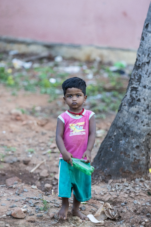PONDICHERY, PUDUCHERRY, TAMIL NADU, INDIA - March circa, 2018. Unidentified Small indian barefoot boy in worn out poor clothes playing with a plastic bottle in the street.のeditorial素材