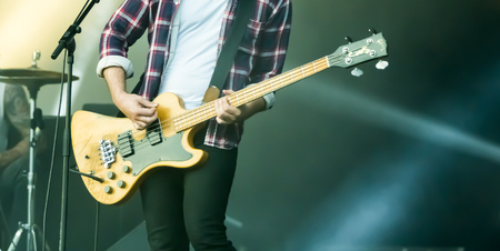 Man guitarist bass guitar instrument performing at stage rock music. Scene outdoor light. Authentic...