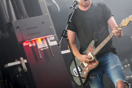 Man guitarist bass guitar instrument performing at stage rock music. Scene outdoor light. Authentic...