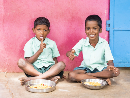 PUDUCHERRY, TAMIL NADU, INDIA - DECEMBER Circa, 2018. Two Unidentified poor classmates boys with uniforms sitting on the floor outdoors, eating with their right hand some rice with masala. Lunch time, unhealthy food in public government schoolのeditorial素材