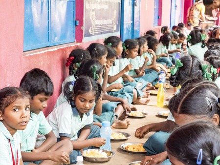 PUDUCHERRY, TAMIL NADU, INDIA - DECEMBER Circa, 2018. Unidentified poor classmates children group with uniforms sitting on the floor outdoors, eating with their right hand some rice with masala. Lunch time, unhealthy food in public government schoolのeditorial素材