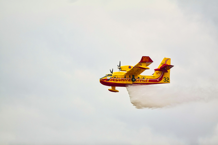 LE BOURGET, FRANCE - JUNE 24, 2017. Small yellow red seaplane hydroplane flying in the sky with clouds droping water at International aeronautical and spatial meeting nearParisのeditorial素材