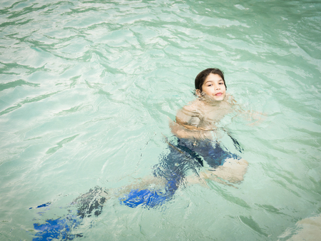 Cheerful teenager boy swimming in crystal turquoise water at summer time with good sun lightの写真素材