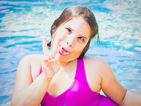 Portrait of a cute teen girl have fun and make faces grimace with fingers and tongue in swimming pool at summer timeの写真素材
