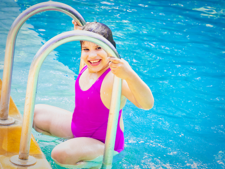 Portrait of cute little indian french girl in the swimming pool, happy child having fun in water,...