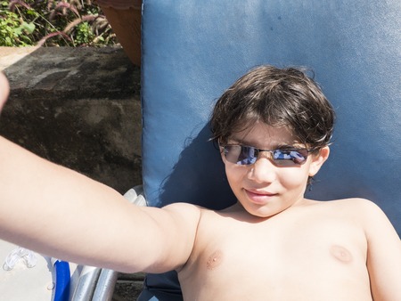 happy teenage boy in sunglasses lying on sunbath and taking selfie at summer time during vacationsの写真素材
