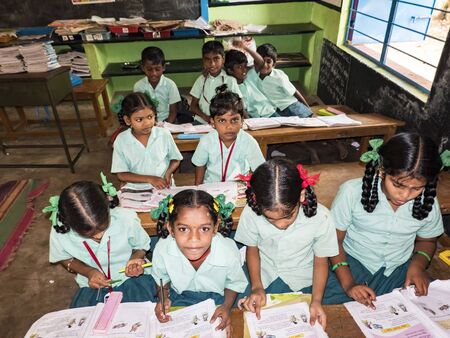 PUDUCHERRY, INDIA - DECEMBER Circa, 2018. Unidentified happy classmates in government school uniforms sitting, studying reading books indoors classroom. Portrait of school teenagers enjoying friendship emotion.のeditorial素材