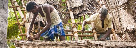 PUDUCHERRY, TAMIL NADU - DECEMBER Circa, 2018. Unidentified Indian workers covered the top of the log cabin with coconut leaves to serve tourists. Hard job for Dalit peopleのeditorial素材