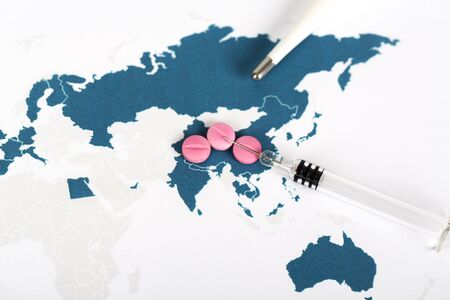 Novel Covid-19, virus concept . World map paper with blue countries infected by virus, on white background. Copy space. with thermometer, pills, syringe.の写真素材
