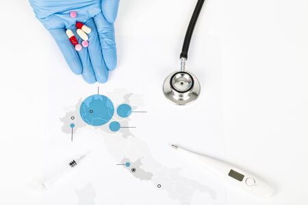 Novel Covid-19, Italy map paper with blue areas infected by virus, on white background. Copy space. with human hand with blue gloves and thermometer, pills, syringe, stethoscopeの写真素材
